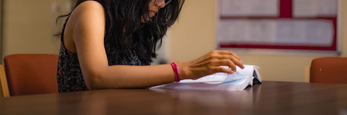 A student reading a textbook at a table, working through it by hand.